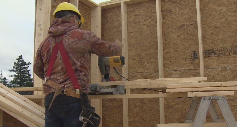 A carpenter using a saw to cut wooden boards. 