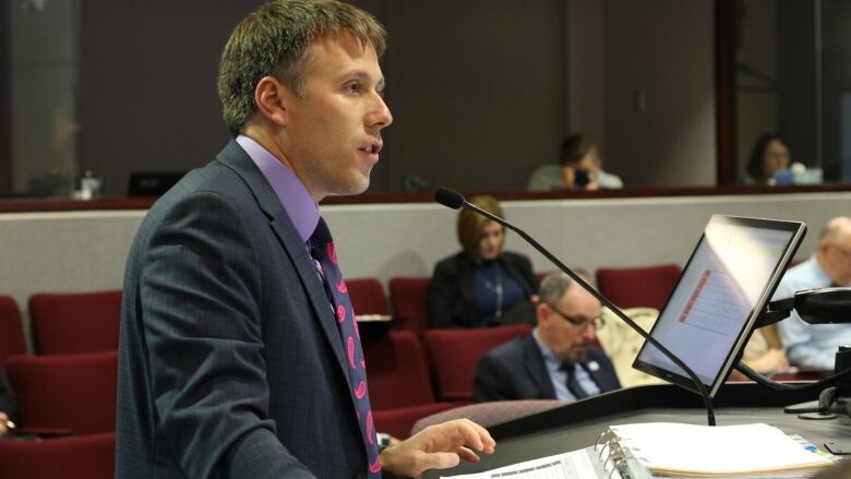 A man in a dark coloured suit standing at a podium speaking. 