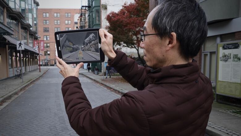 Henry Tsang, creator of 360 Riot Walk, shows the tour on a tablet while standing at one of the stops in Shanghai Alley, the centre of the city's original Chinatown.