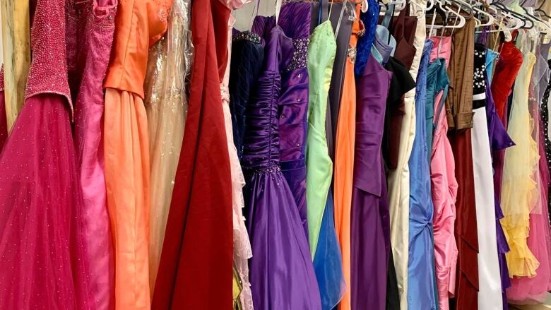 Beautiful prom gowns hung up on a rack. One of every colour of the rainbow. 