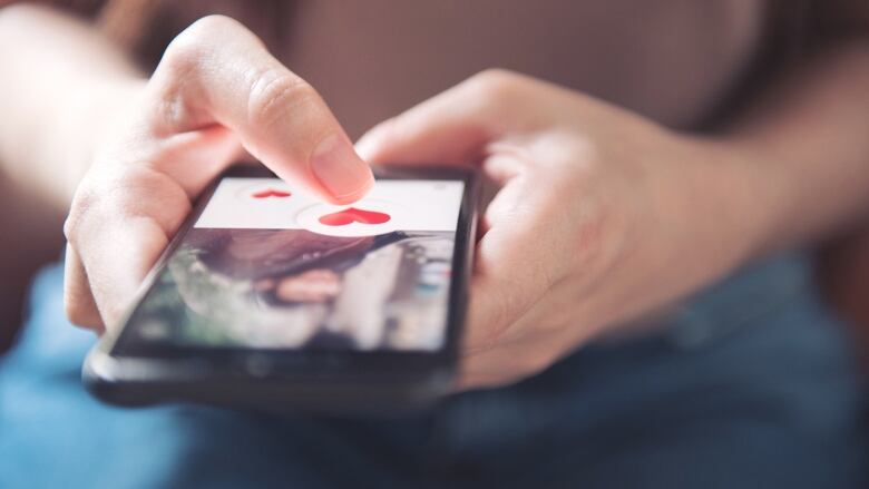 Stock image of hands holding a smartphone with a heart on it, indicating a dating app.