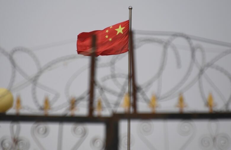 A Chinese flag is seen behind a fence topped with razor wire.