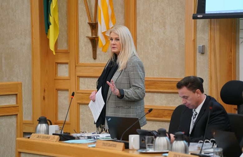 A woman stands behind a table during a meeting.