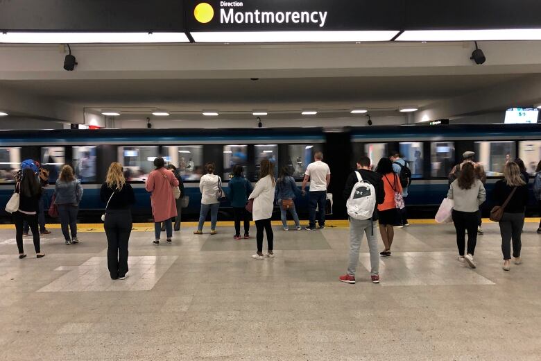 People stand in a busy subway station as a train passes by.