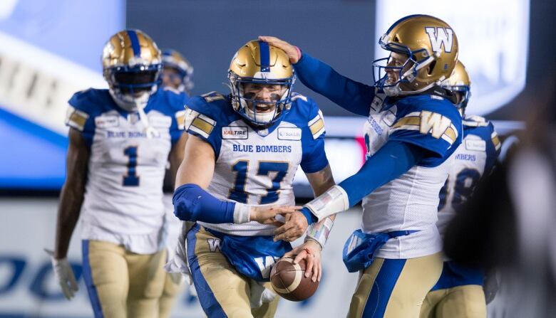 A football taps another football player's head as he holds a football. 