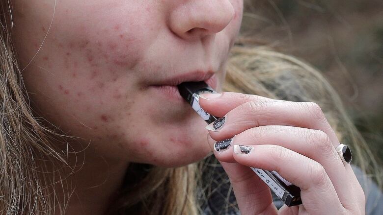 A young woman uses a vaping device.