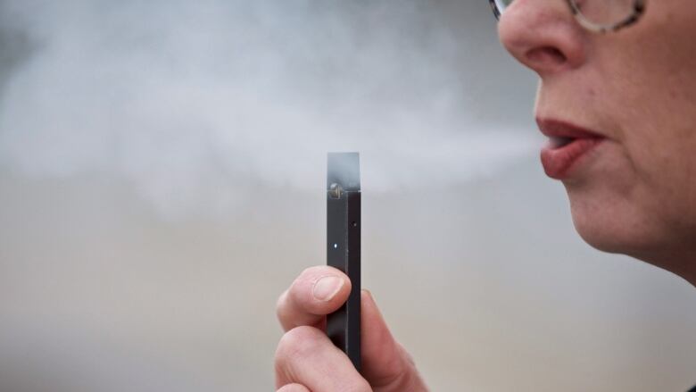 A woman holds an e-cigarette device and exhales a puff of vapor.