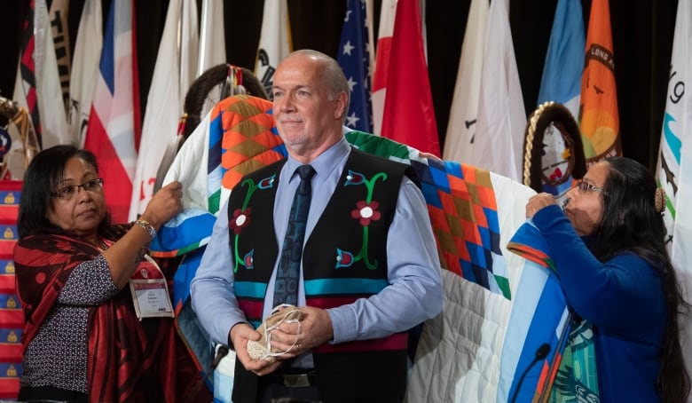 John Horgan is presented with a blanket by two Indigenous women during a ceremony.