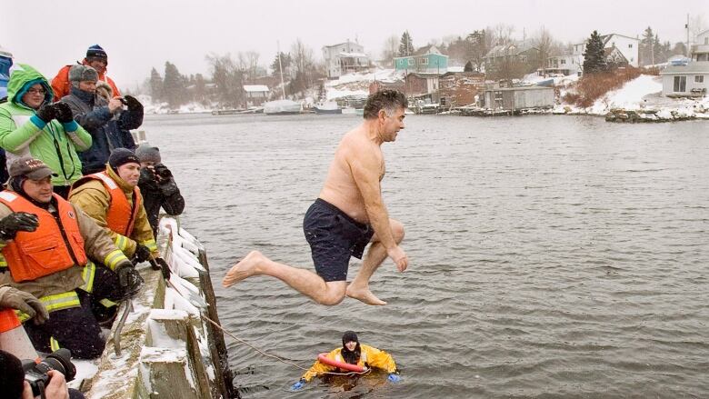 Man in swimsuit jumps into water as people in winter gear look on