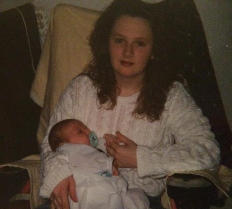 A young woman with curly hair holds a newborn baby. 