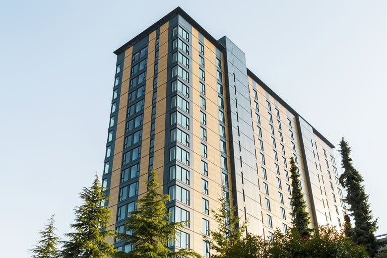 An 18-storey building with a wood exterior is flanked by pine trees. 