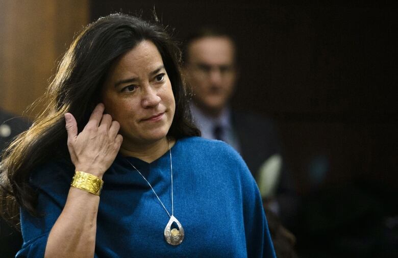 A woman in a blue sweater walks into a meeting.