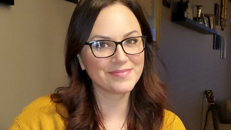 A woman wearing glasses holds a green mug and smiles at the camera.