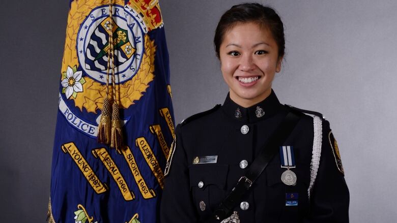 A woman in a police uniform smiles as she stands next to a flag of the Vancouver Police Department.