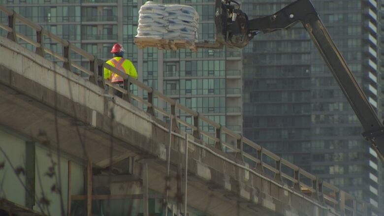 A construction person is seen on top of a highway. Machinery is pictured in the background.