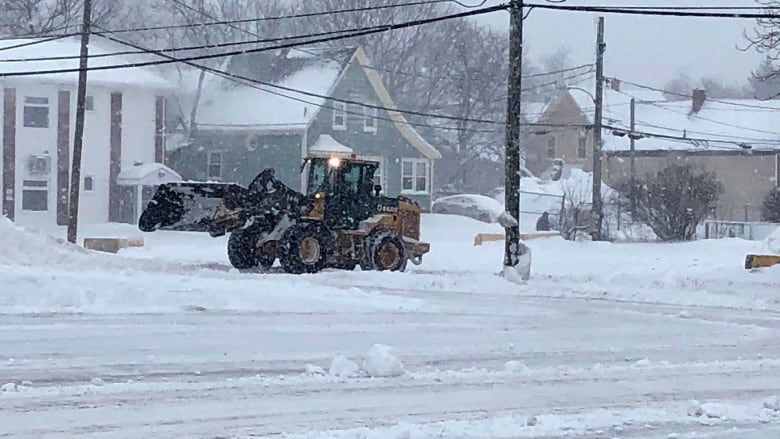 A tractor with a snowplow on the front plows snow on a city street