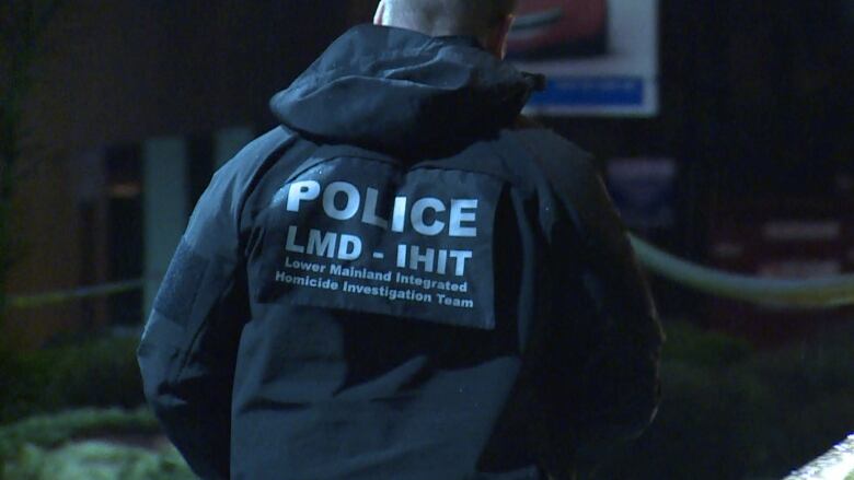 A picture of the back of a police officer. He is wearing a jacket that reads ' Police LMD -IHIT Lower Mainland Integrated Homicide Investigation Team'.