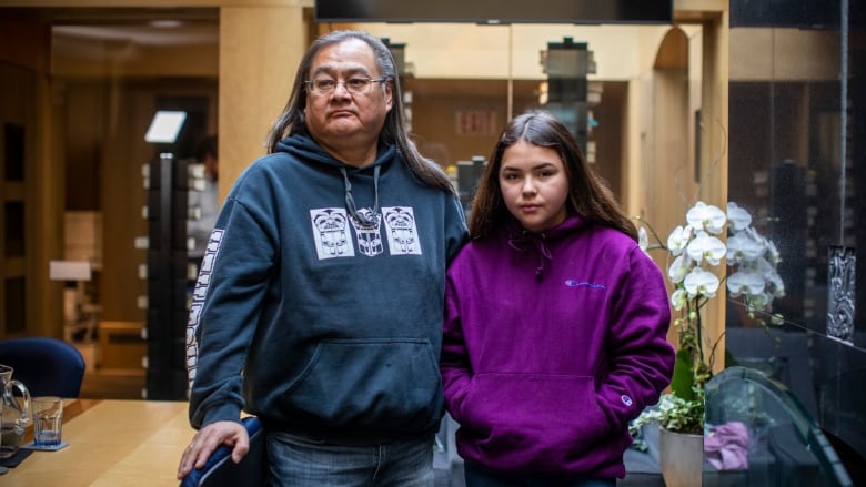 An Indigenous man and a young girl, both wearing hoodies, pose for a picture in an office-like building.