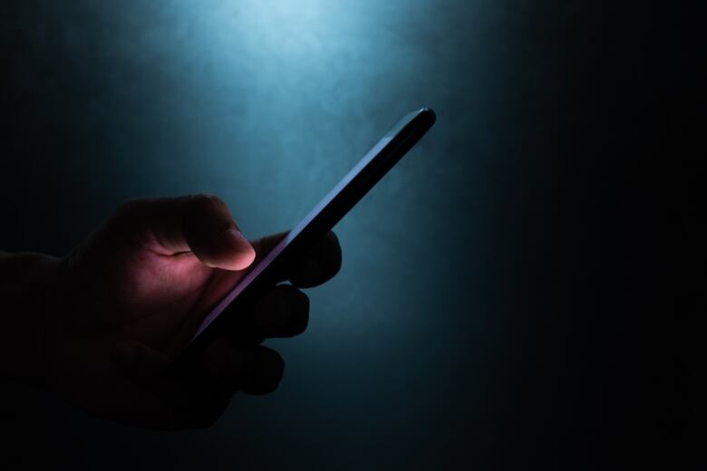 A person's hand is seen holding a mobile device in the dark.