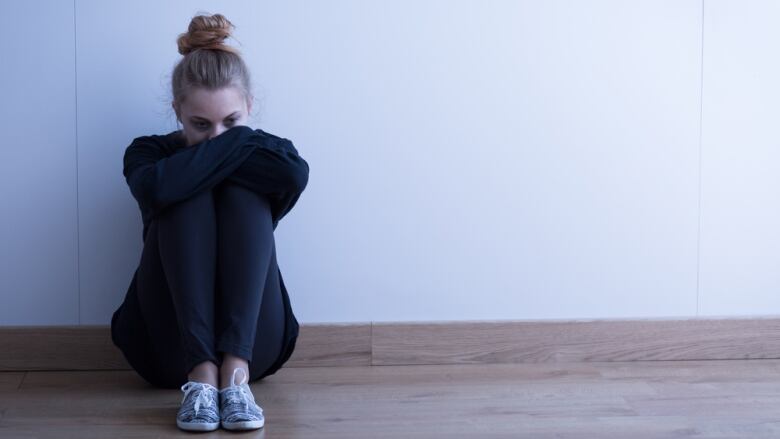 A young woman sits on the floor with her head resting on her knees.