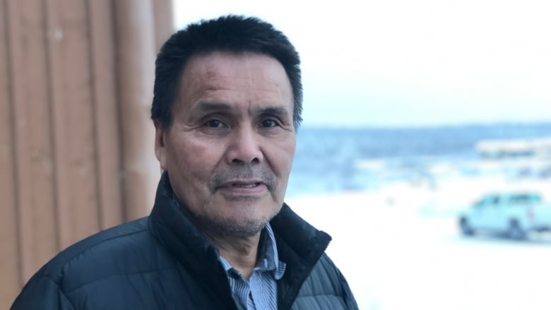 Man standing near a structure with snow in the background.