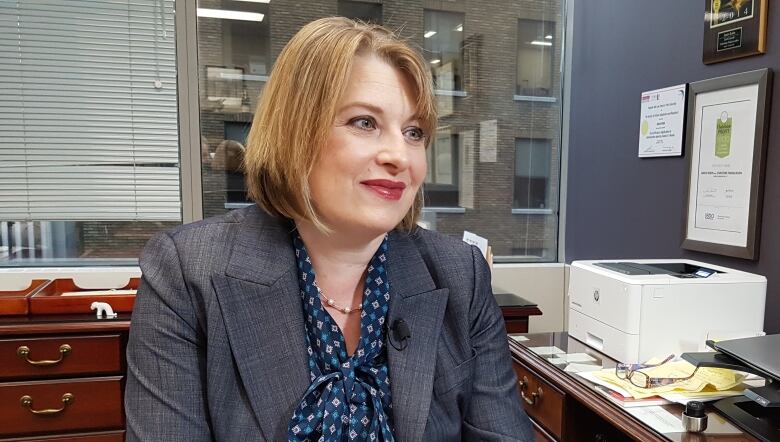 Woman in business blazer sits at desk.