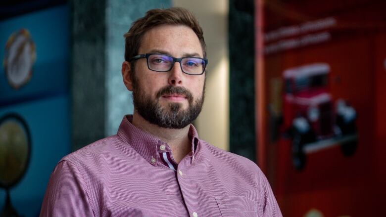 A man in a collared shirt and glasses poses for a photo indoors.