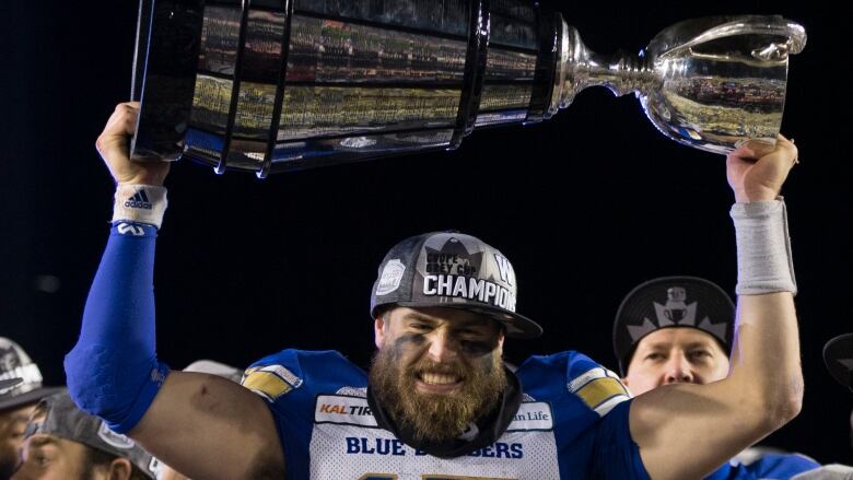 A man holds a large silver trophy over his head