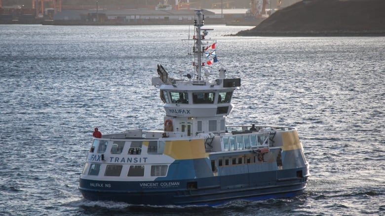 A blue and yellow Halifax Transit ferry crosses the Halifax harbour on a sunny day.