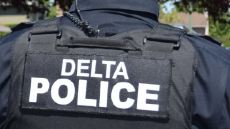 The back of a Delta police officer, wearing a vest with the words Delta Police.