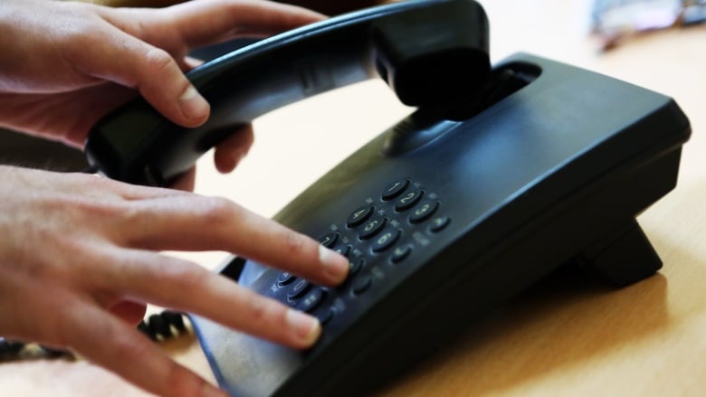 A closeup shows a hand dialling numbers on a landline phone.