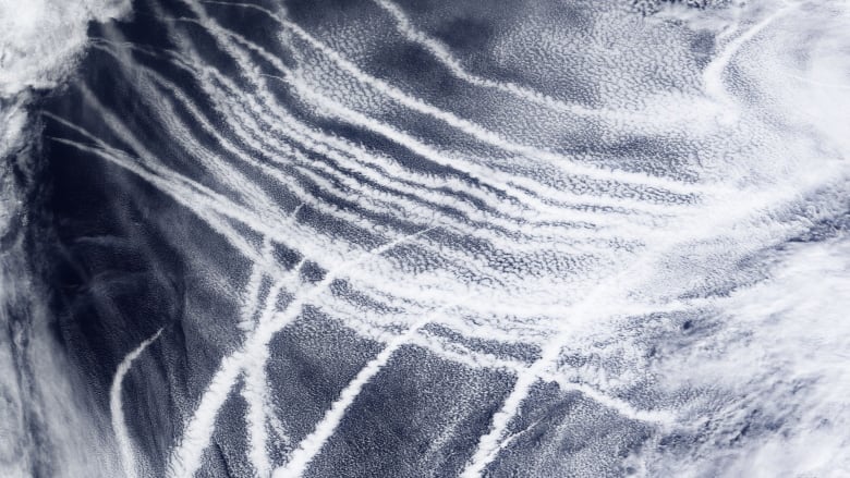 A satellite image shows clouds and what look like contrails in near parallel lines above a dark-blue ocean.