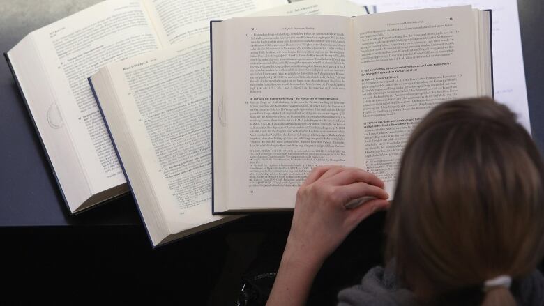 Woman reading from a university textbook stacked on top of other textbooks