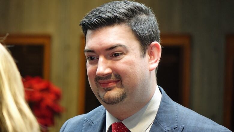 A man with a goatee wears a blazer and red tie. 