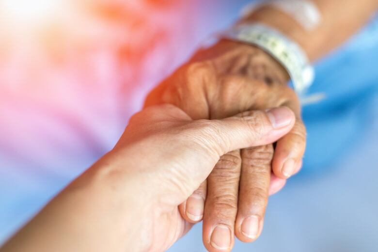 A younger hand clasps the hand of a senior.