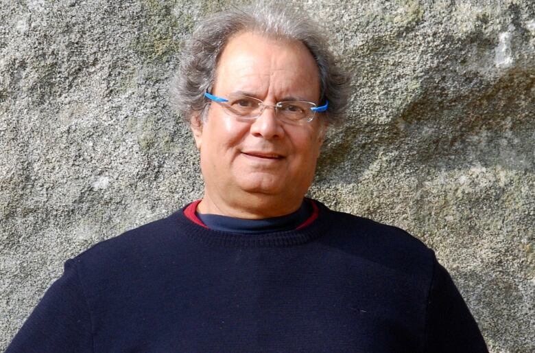 A portrait of a man standing in front of a stone facade.