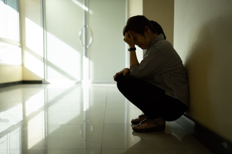 A woman in shadows holds her head in her hands.