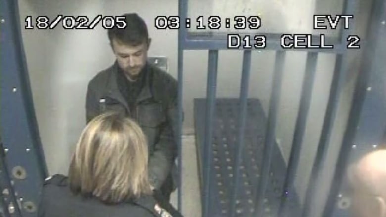 A man in a black jacket stands in a cell.