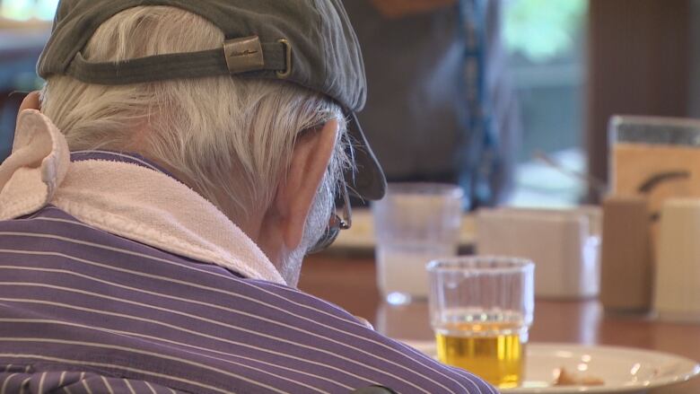 The back of a man's head who has grey hair and is eating a meal.