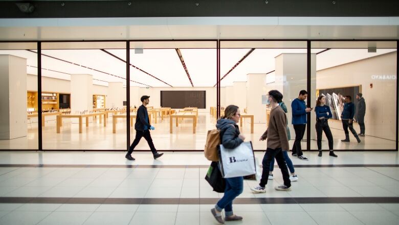 Three people walk in opposite directions, one woman has a big white bag with the words 