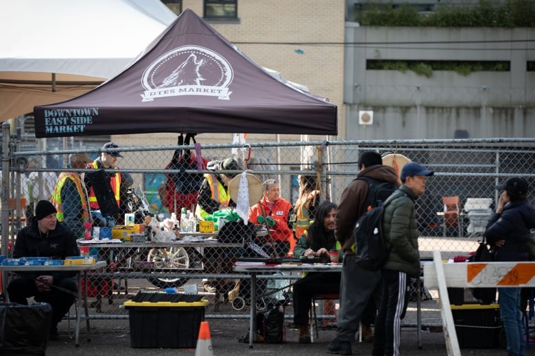 A group of people are seen at outdoor stalls.