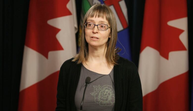 A woman addresses the media in front of the flags of Canada and Alberta.