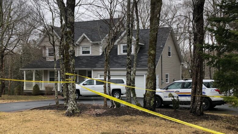 A large home with yellow police tape around it. Two police vehicles are seen in the driveway.