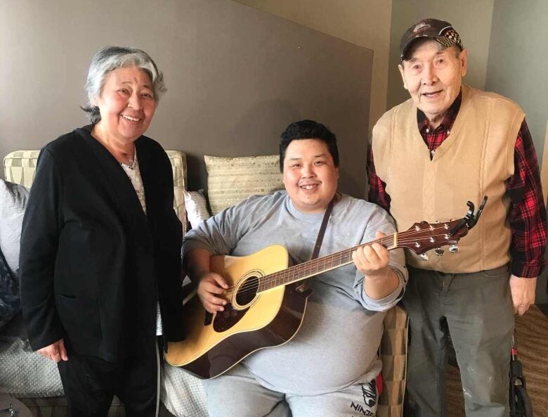 Three people, a couch and a guitar.