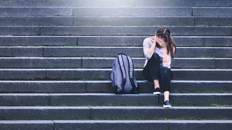 Someone sitting on staircase with head in hands, with purple backpack.