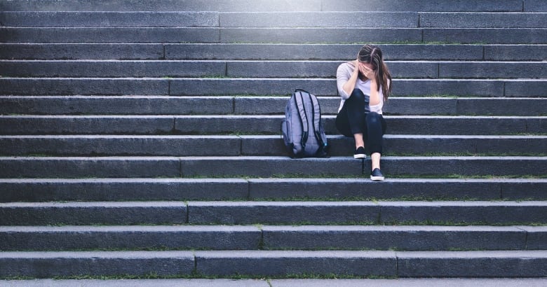 Someone sitting on staircase with head in hands, with purple backpack.