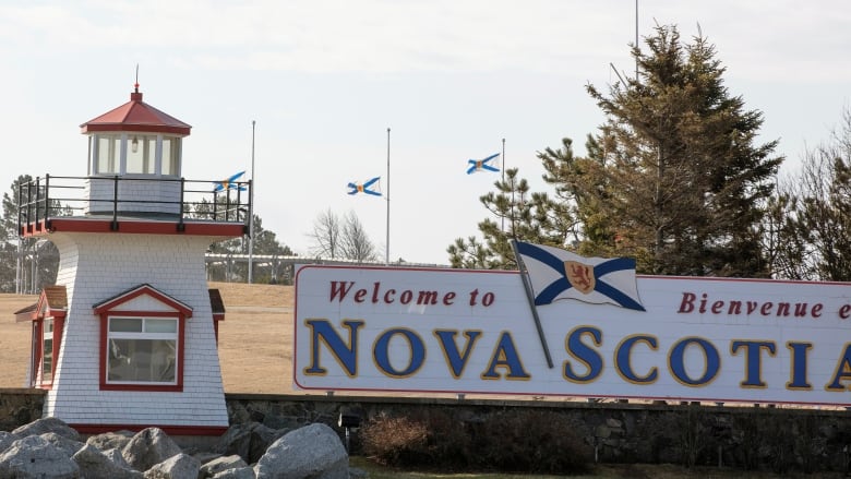 A small lighthouse stands beside a sign that says 'Welcome to Nova Scotia.'