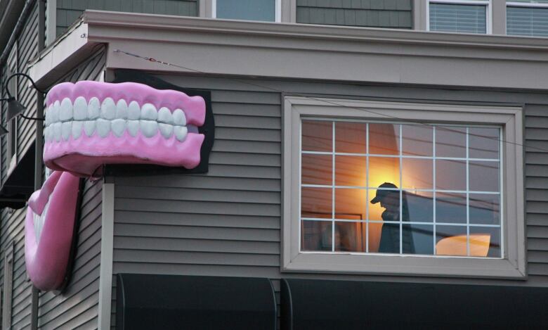 A grey building is shown with a large pair of teeth displayed on the corner advertising it as a denture clinic.