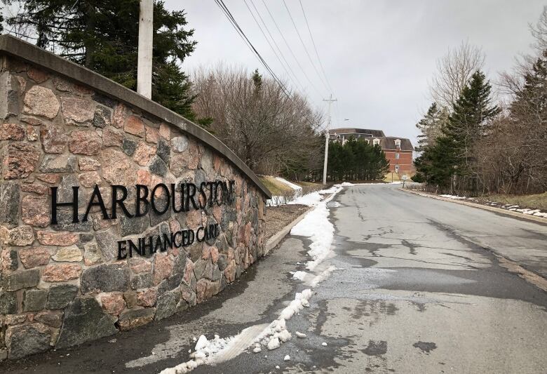 The entrance to the Harbourstone facility is shown, with a stone wall on the left and a driveway leading to the care home in the distance.