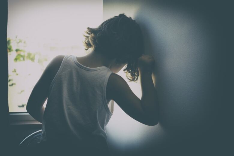 A child with curly hair sits in a window. The child is turned away from the camera.